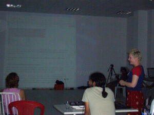 Photo of three people in a seminar room with a computer screen projected on a wall